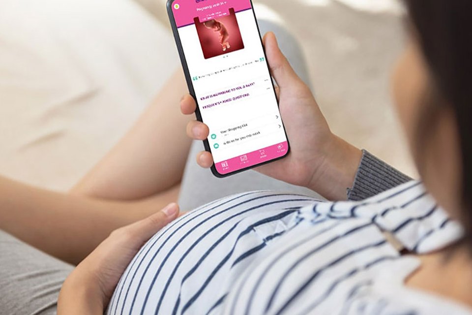 A pregnant lady scrolling through the Emma's Diary app on her phone.